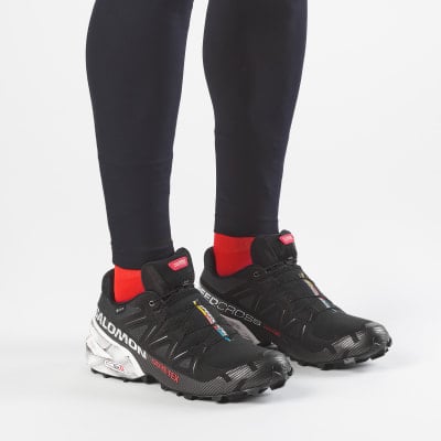 Schwarze Salomon-Laufschuhe mit roten Socken und dunklen Leggings. Schwarze Salomon-Laufschuhe mit roten Socken und dunklen Leggings.