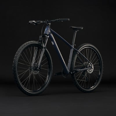 Dunkelblaues Mountainbike mit schwarzen Rädern und Federung auf dunklem Hintergrund.