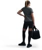 Eine Frau in schwarzer Kleidung hält eine Sporttasche und steht auf weißem Hintergrund.