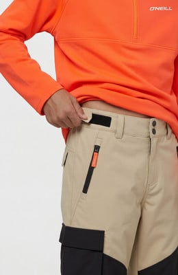 Ein Mann trägt ein orangefarbenes Sweatshirt und eine beige Hose mit schwarzen Details.