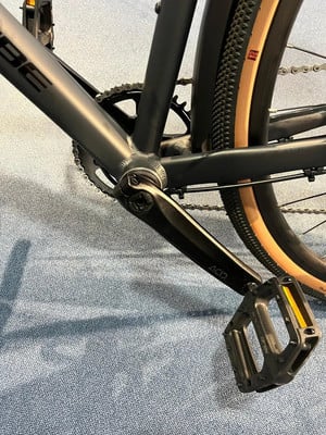 Nahaufnahme eines Fahrradpedals und einer Kurbel auf dunklem Untergrund.