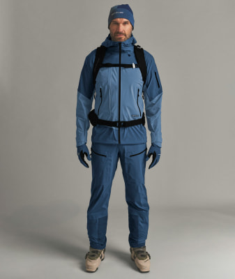 Ein Mann in blauer Skibekleidung mit Rucksack und Skischuhen.