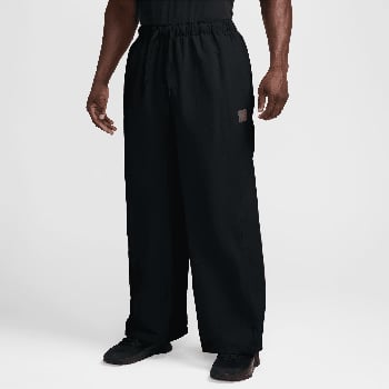 Ein Mann trägt eine schwarze, weite Hose mit einem Logo auf dem linken Oberschenkel.
