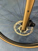 Detail eines Fahrradrades mit Scheibenbremse und goldener Gabel.