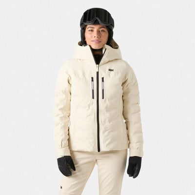 Eine Frau in einer beigefarbenen Skijacke und Hose mit Helm und Brille. Eine Frau in einer beigefarbenen Skijacke und Hose mit Helm und Brille.