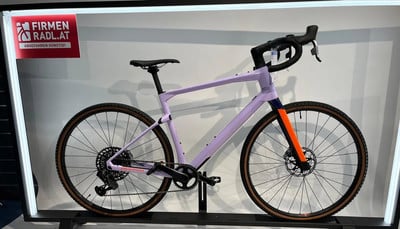 Lila Gravelbike mit orangefarbener Gabel und braunen Reifen auf Ständer. Lila Gravelbike mit orangefarbener Gabel und braunen Reifen auf Ständer.