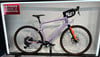 Lila Gravelbike mit orangefarbener Gabel und braunen Reifen auf Ständer.