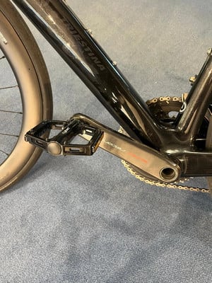 Detail eines schwarzen Fahrrads mit Kurbel und Pedal auf blauem Teppich. Detail eines schwarzen Fahrrads mit Kurbel und Pedal auf blauem Teppich.