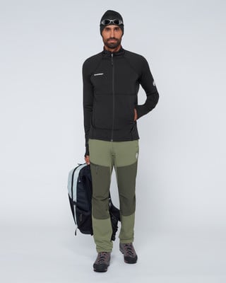 Ein Mann in schwarzer Kleidung und grüner Hose hält einen Rucksack. Ein Mann in schwarzer Kleidung und grüner Hose hält einen Rucksack.