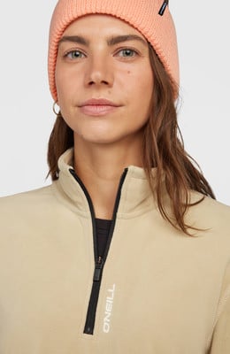 Ein Mädchen in einer rosa Mütze und einem beigen Fleece-Pullover mit O'Neill-Logo. Ein Mädchen in einer rosa Mütze und einem beigen Fleece-Pullover mit O'Neill-Logo.