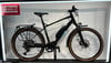 Schwarzes E-Bike mit Gepäckträger und braunen Reifen steht auf einer Ausstellung.