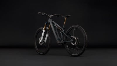 Ein graues Mountain-E-Bike mit Federung und schwarzen Rädern auf dunklem Hintergrund.