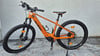 Ein orangefarbenes KTM E-Bike mit dicken Reifen steht auf grauem Untergrund.