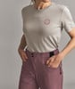 Eine Frau in einem grauen T-Shirt mit Logo und einer rosafarbenen Hose mit Taschen.