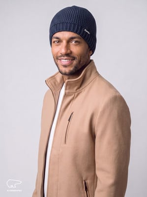 Ein Mann in einer dunkelblauen Mütze und einer beigen Jacke lächelt. Ein Mann in einer dunkelblauen Mütze und einer beigen Jacke lächelt.