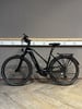 Ein schwarzes KTM E-Bike steht auf einem Holzboden vor einer grauen Wand.