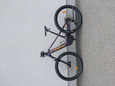 Ein lila Mountainbike der Marke LAPIERRE steht an einer grauen Wand.
