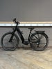 Ein schwarzes KTM E-Bike steht auf einem Holzboden vor einer grauen Wand.