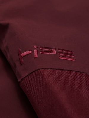 Logo-Detail auf dunkelweinrotem Stoff mit Textur und Falten. Logo-Detail auf dunkelweinrotem Stoff mit Textur und Falten.