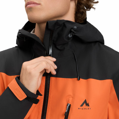 Ein Mann schließt eine orange-schwarze McKinley-Jacke mit Kapuze. Ein Mann schließt eine orange-schwarze McKinley-Jacke mit Kapuze.