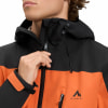 Ein Mann schließt eine orange-schwarze McKinley-Jacke mit Kapuze.