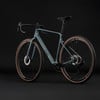 Modernes Gravelbike mit glänzendem Rahmen und braunen Reifen vor schwarzem Hintergrund.