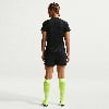 Eine Frau in schwarzem Shirt, Shorts und neongelben Socken steht rückwärts.