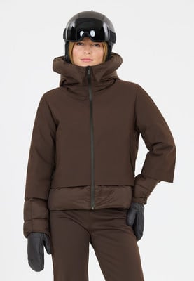 Eine Frau in einer braunen Skijacke, Helm und Brille steht vor weißem Hintergrund. Eine Frau in einer braunen Skijacke, Helm und Brille steht vor weißem Hintergrund.