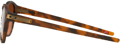 Brille in Schildpattoptik mit orangefarbenen Gläsern und goldenem Oakley-Logo.