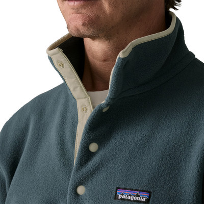 Detail eines Mannes in einer dunkelblauen Fleecejacke mit beiger Paspel und Patagonia-Logo. Detail eines Mannes in einer dunkelblauen Fleecejacke mit beiger Paspel und Patagonia-Logo.