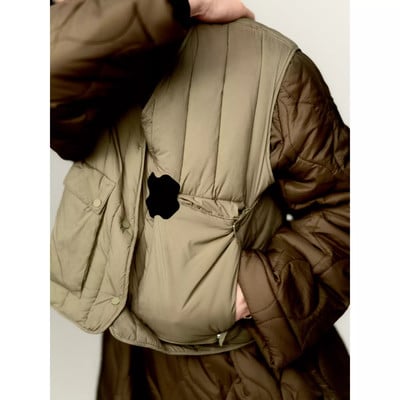 Eine Person hält eine beige gesteppte Weste über einer braunen gesteppten Jacke.