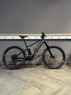 Ein schwarzes Scott E-Mountainbike steht auf einem Holzboden vor einer grauen Wand. Ein schwarzes Scott E-Mountainbike steht auf einem Holzboden vor einer grauen Wand.