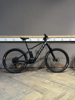 Ein schwarzes Scott E-Mountainbike steht auf einem Holzboden vor einer grauen Wand.