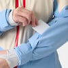 Eine Hand steckt eine weiße Karte in eine Ärmeltasche einer Jacke.
