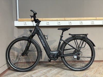 Ein schwarzes E-Bike mit Schutzblechen und Gepäckträger steht auf Holzboden. Ein schwarzes E-Bike mit Schutzblechen und Gepäckträger steht auf Holzboden.