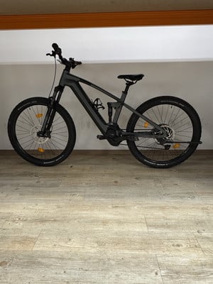 Ein graues E-Mountainbike mit Federung steht auf Holzboden. Ein graues E-Mountainbike mit Federung steht auf Holzboden.