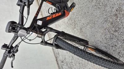 Ein schwarzes KTM E-Bike mit orangefarbenem Logo auf dem Rahmen steht auf dem Boden. Ein schwarzes KTM E-Bike mit orangefarbenem Logo auf dem Rahmen steht auf dem Boden.