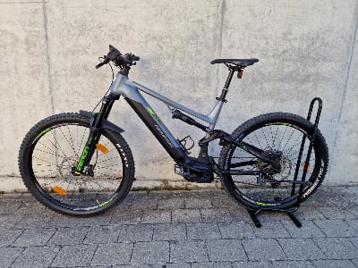 Ein Genesis E-Mountainbike mit Federung und Schutzblechen steht auf Pflastersteinen. Ein Genesis E-Mountainbike mit Federung und Schutzblechen steht auf Pflastersteinen.
