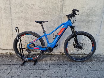 Ein blaues Mountain-E-Bike steht auf einem Ständer vor einer Betonwand.