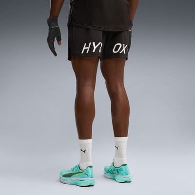 Ein Mann in schwarzen Shorts mit HYROX-Aufschrift und grünen Laufschuhen.
