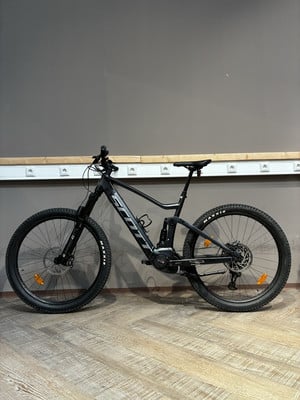 Ein schwarzes Scott Mountain E-Bike mit Federung steht auf einem Holzboden. Ein schwarzes Scott Mountain E-Bike mit Federung steht auf einem Holzboden.