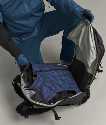Ein Mann packt eine blaue Daunenjacke in einen Rucksack, bekleidet mit blauer Kleidung. Ein Mann packt eine blaue Daunenjacke in einen Rucksack, bekleidet mit blauer Kleidung.