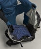Ein Mann packt eine blaue Daunenjacke in einen Rucksack, bekleidet mit blauer Kleidung.