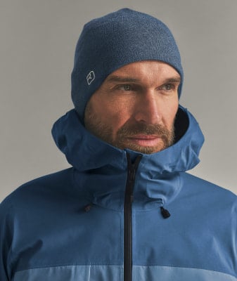 Mann in blauer Winterjacke und Mütze mit Logo.