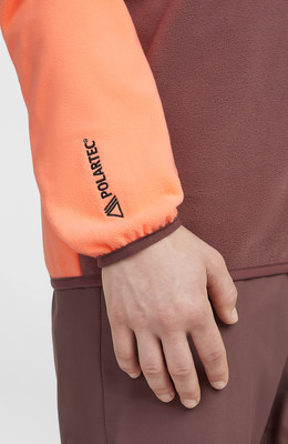 Hand in orange Ärmel mit Polartec-Logo, Teil einer braunen Jacke. Hand in orange Ärmel mit Polartec-Logo, Teil einer braunen Jacke.