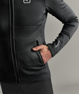 Ein Mann steckt seine Hand in die Tasche einer schwarzen Jacke mit einem Logo auf der Brust. Ein Mann steckt seine Hand in die Tasche einer schwarzen Jacke mit einem Logo auf der Brust.