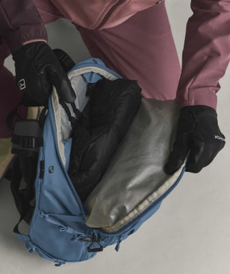 Eine Person in Handschuhen verstaut Kleidung in einem blauen Rucksack.