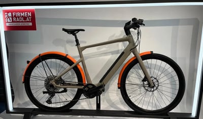 Modernes E-Bike in Grau mit orangen Schutzblechen und Firmenlogo.