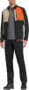Ein Mann in einer Outdoor-Jacke und -Hose mit Berglogo und orangefarbenen Akzenten.