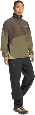 Ein Mann in einem braun-grünen Fleece-Pullover und schwarzer Hose mit Adidas-Logo.